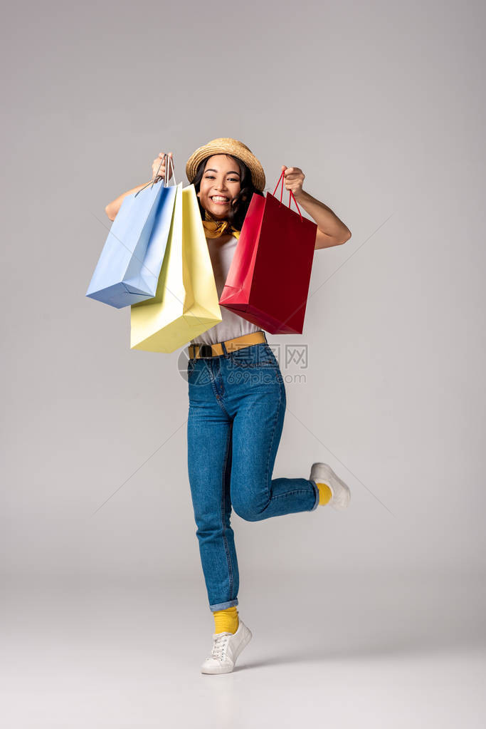 穿着时装的欢快潮情快乐身着亚洲女拿着五花八门的购物袋在灰图片