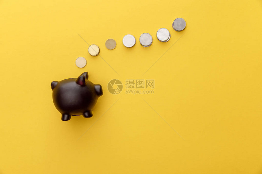 黄色背景硬币的黑色存钱罐的顶部视图图片