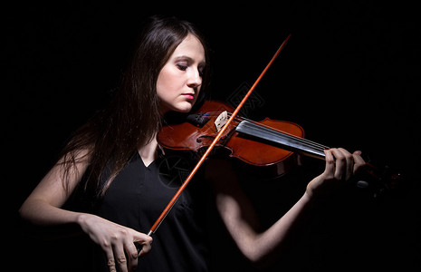 黑发女人在黑色上演奏小提琴图片