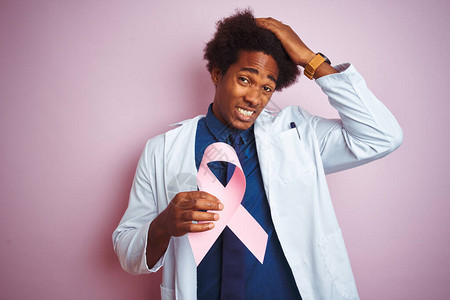 年轻的美国黑人医生拿着癌症丝带站在孤立的粉红色背景上图片