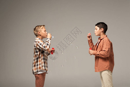 两兄弟在灰色上吹肥皂泡的侧视图图片
