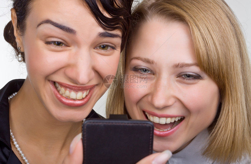 两个近身笑着看轻背景的手机的女人图片
