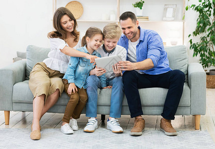 幸福的一家四口使用平板电脑一起坐在家里的沙发上图片
