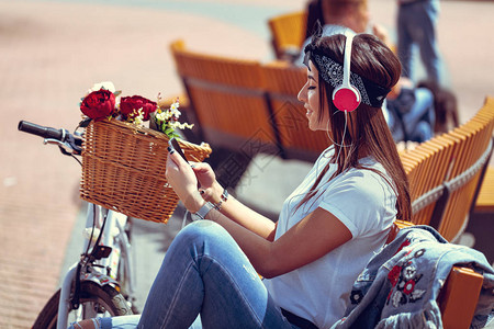 城市里年轻女士坐在长椅听着音乐图片