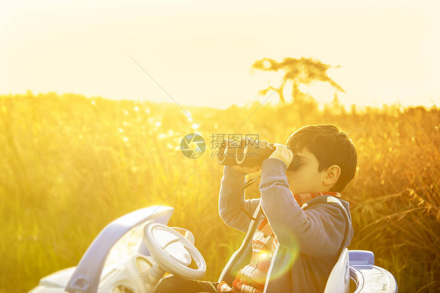 日落时分坐在玩具车里的小男孩拿着望远镜看向远方图片