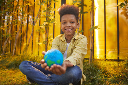 笑的非裔美国男孩在阳光下坐在绿草地上时将握在手边图片
