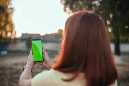 带着背的年轻女孩在公园里用智能手机拍自图片
