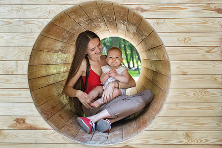 母亲和孩子坐在游乐场的木制隧道里快乐图片
