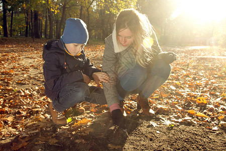 男孩和母亲在秋天公园的地上写着一些东西图片
