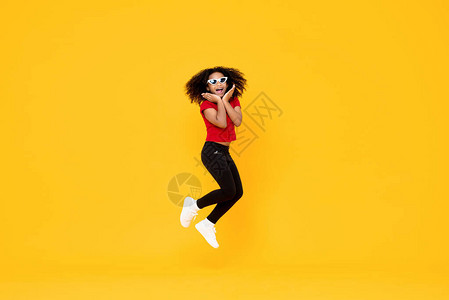 尼日利亚人快乐的时尚非裔美国女孩在空中跳跃用手抓着黄背景背景