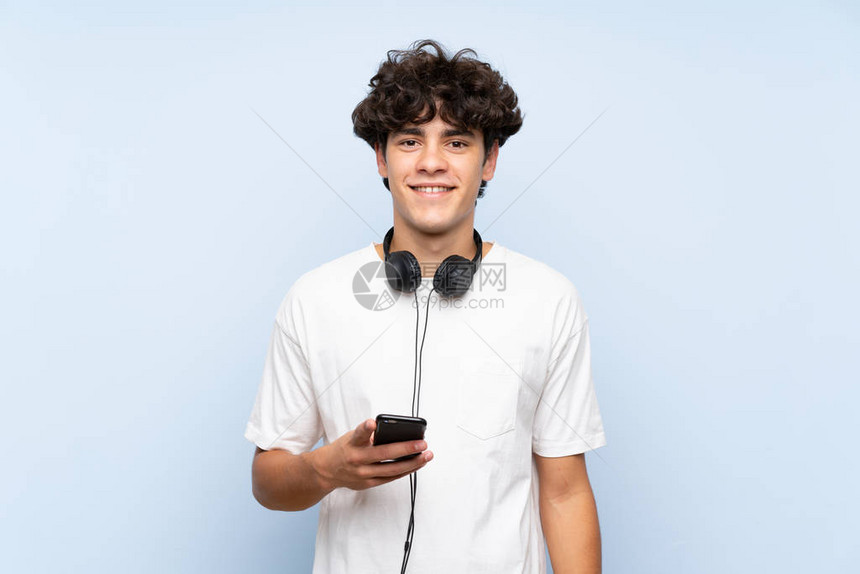 年轻男子听音乐与移动手机超过隔绝的蓝色墙壁图片