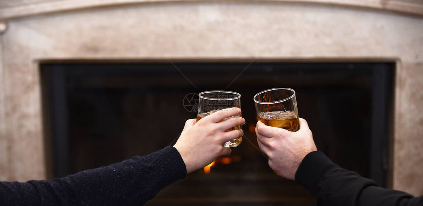 男手中的威士忌酒杯手在壁炉背景上叮当作响的威士忌酒杯在家里壁炉旁的眼镜里拿着饮料的男手男人们在壁炉旁的眼镜里图片
