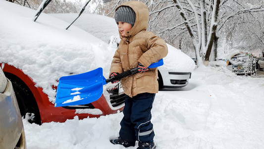 穿着夹克的男孩用大蓝铲子在暴风雪过后帮图片