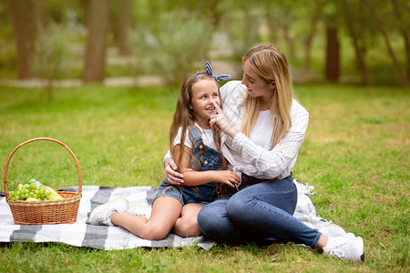 年轻母亲触摸女儿的鼻子在暑假周末一起在公园外面玩彩虹花时间图片