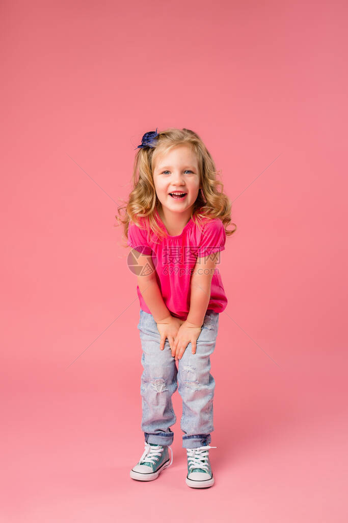 穿着粉红色T恤衫和穿粉红背景牛仔裤的可爱金发小女孩将空间照片复制为文图片