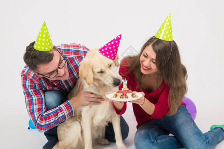 年轻的家庭带着他们的狗金毛猎犬庆祝一周岁生日友谊爱家庭在白色背景图片