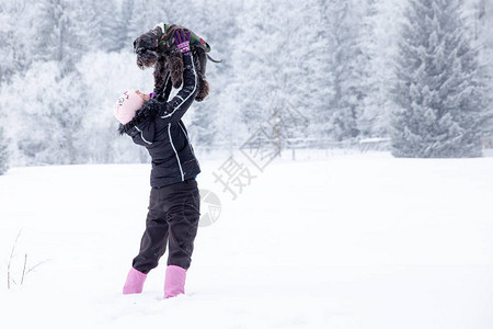 年轻女子在冬天的雪上玩黑小狗图片