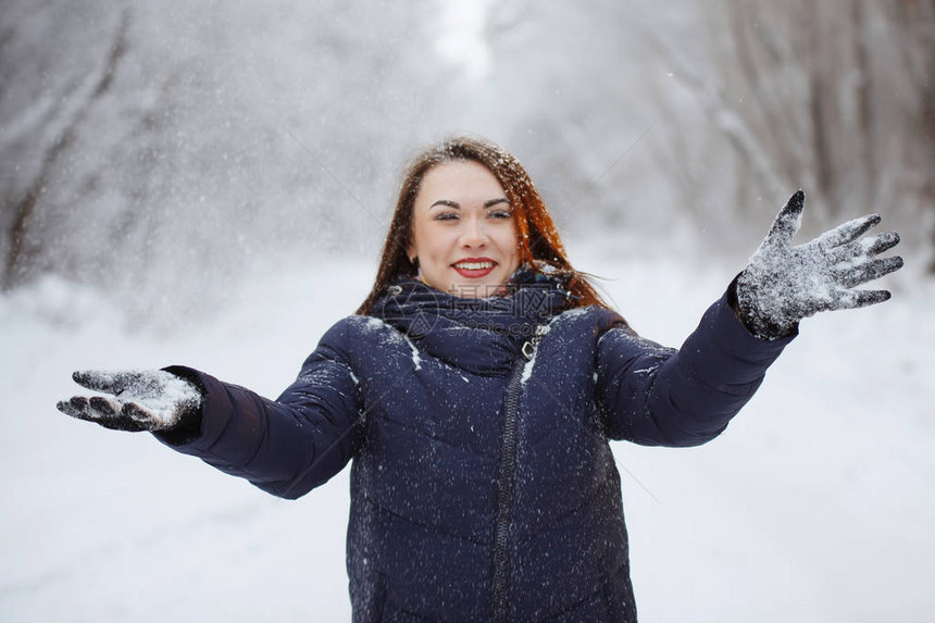 穿蓝围巾和长发外套的漂亮女人在雪林里把雪花扔到新鲜空气中青春图片