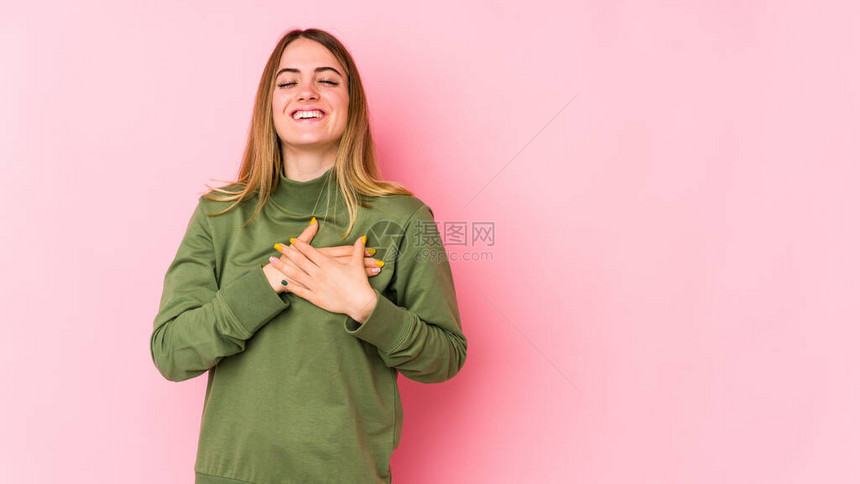 年轻的caucasian女人被孤立在粉红色背景上笑着把双手放在心上图片