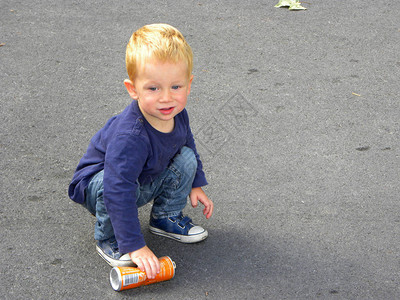 一个金发的小孩蹲在人行道上小男孩拿起一个锡图片