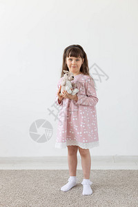 美丽的小女孩拿着一只穿着粉色连衣裙的泰迪兔图片