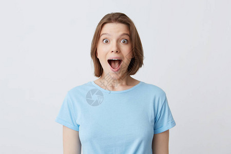 穿着蓝T衬衫张开嘴的快乐年轻女令人惊讶的肖像图片