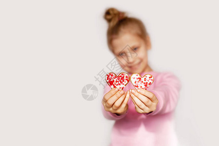 一个快乐的女孩拿着红心形的姜饼可爱女孩的肖像与饼干一起在浅色背景和图片