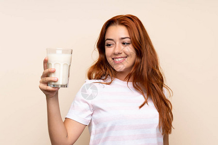 年轻红发女孩拿着一杯牛奶在孤立的背景和快乐的表情上图片