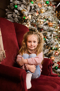 小女孩穿着毛衣和牛仔裤坐在新年树附近背景图片