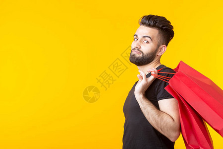 男人拿着黄色背景上的红色购物袋在超市购物和礼品的概图片