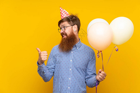 长胡子长胡子的红头男子在孤立的黄色背景上持有气球图片