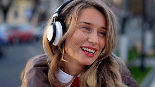 在日落时在街上听无线耳机与手机连通的音乐的快乐妇女图片