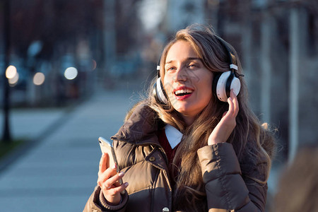 在日落时在街上听无线耳机与手机连通音乐的快乐妇女图片