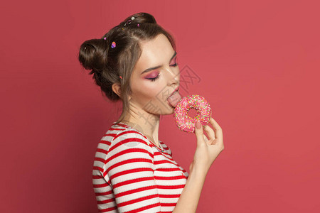 漂亮的女人拿着甜圈在色彩多的粉红背景图片