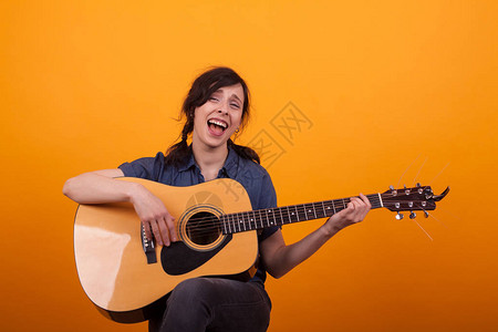 在黄背景的演播室里唱着震动吉他的小歌手和她的吉他一起欢呼图片