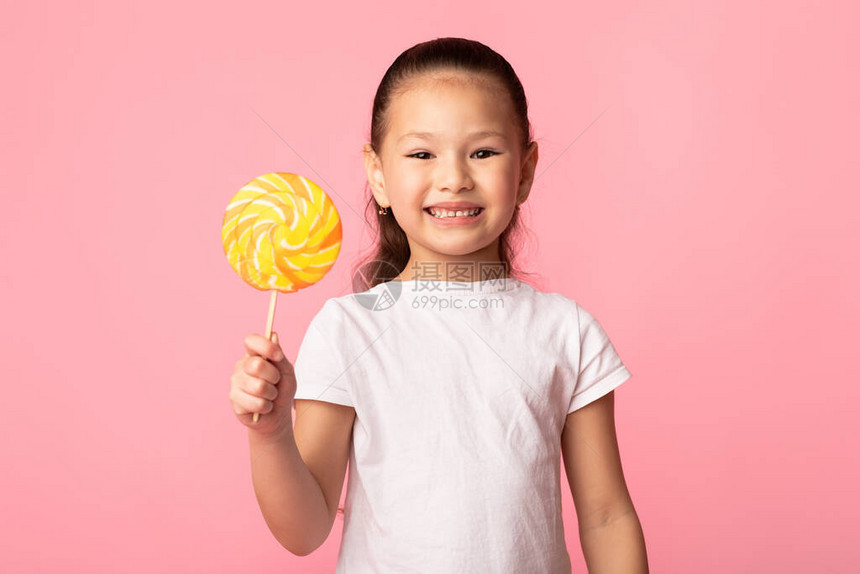 可爱的亚裔女孩笑着拿多彩棒糖被粉红色图片