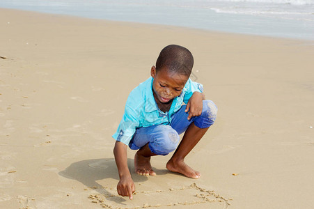 小蹲着的男孩用手指在沙滩上画画图片