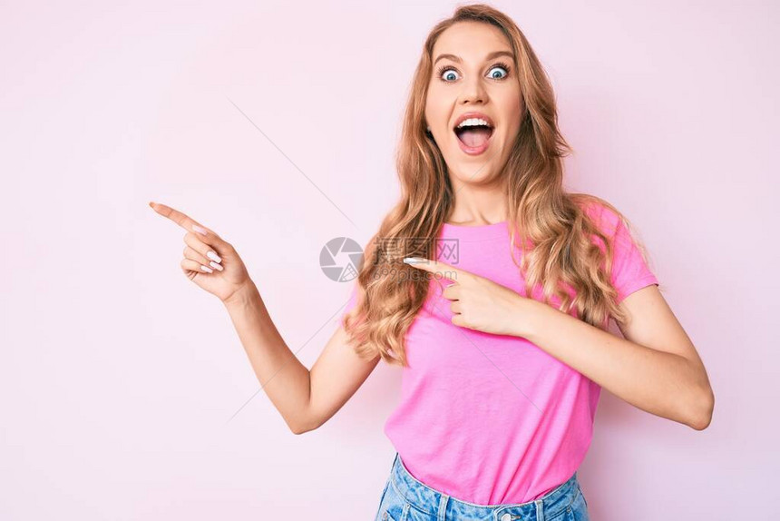 带着金发的年轻caucasian女子用手指对着一边庆祝疯狂和惊异的成功图片
