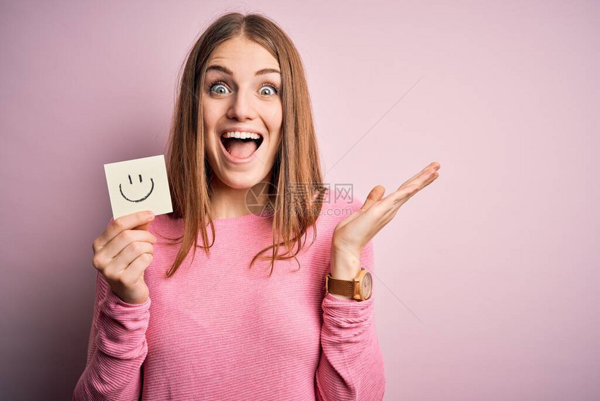 年轻漂亮的红发女人拿着带有微笑表情符号的提醒纸图片