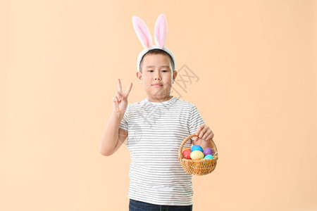 带复活节鸡蛋和耳朵的亚洲小男孩在颜色背景上图片