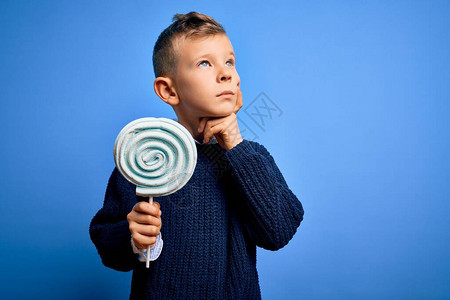 白人小孩在蓝色孤立的背景下吃甜棒糖图片