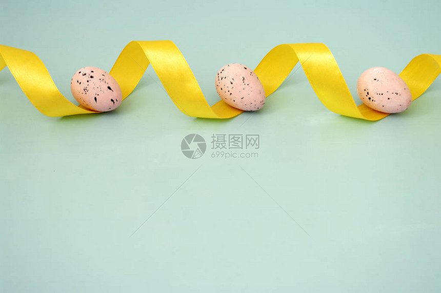 在柔和的蓝色背景上用黄色丝带关闭复活节鹌鹑粉红色鸡蛋复制文本的空间从顶部查看贺卡设图片
