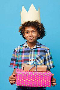 在蓝背景生日派对概念下摆姿势的非洲美籍男孩喜悦的礼物图片