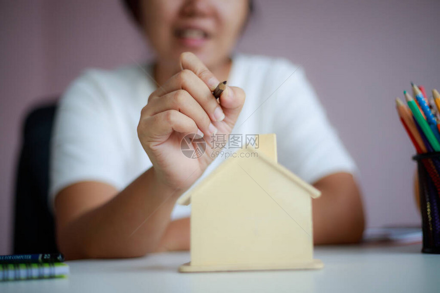 快乐的亚洲女人用铅笔画和用木屋存钱罐比喻计划省钱买房选图片
