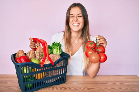 美丽的caucasian女人拿着超市购物篮和西红柿微笑图片