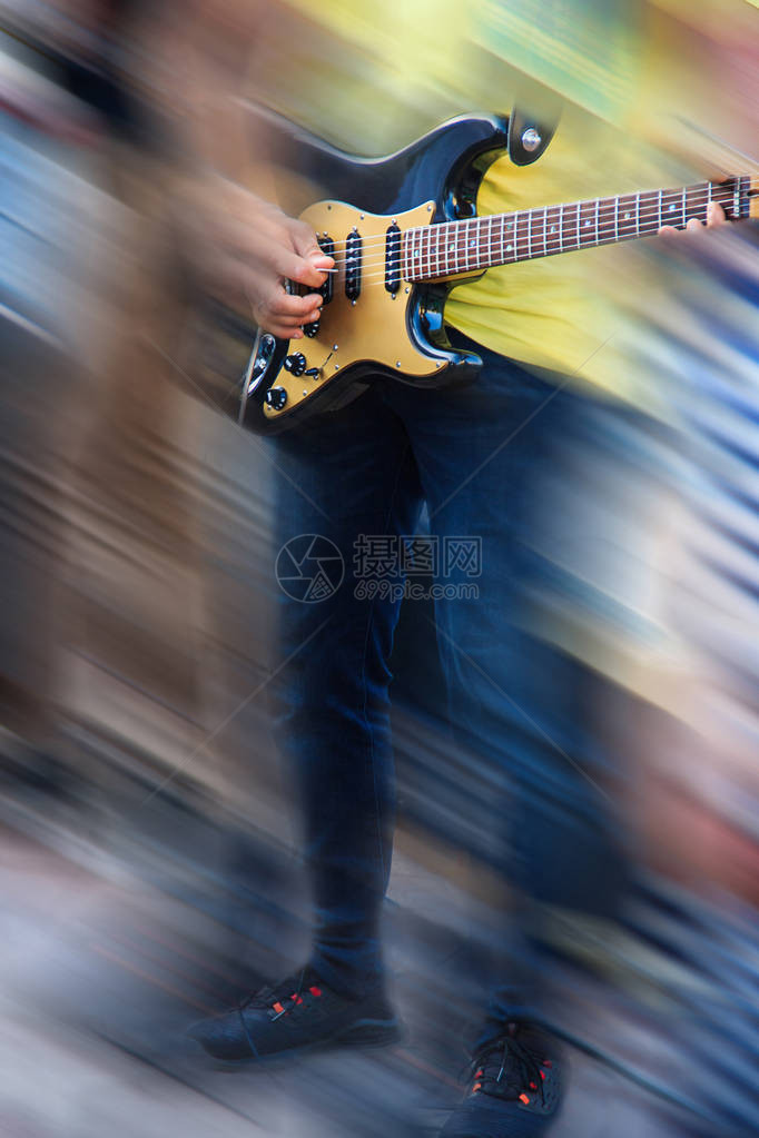 身穿牛仔裤和黄色t恤的吉他手在黑色电吉他上演奏音乐图像的两侧用运动模糊五颜六色的抽象线条模糊音乐教育图片