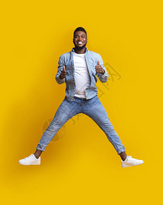 快乐的非洲美国人在空中跳跃他的拇指举高过黄色工作室背图片