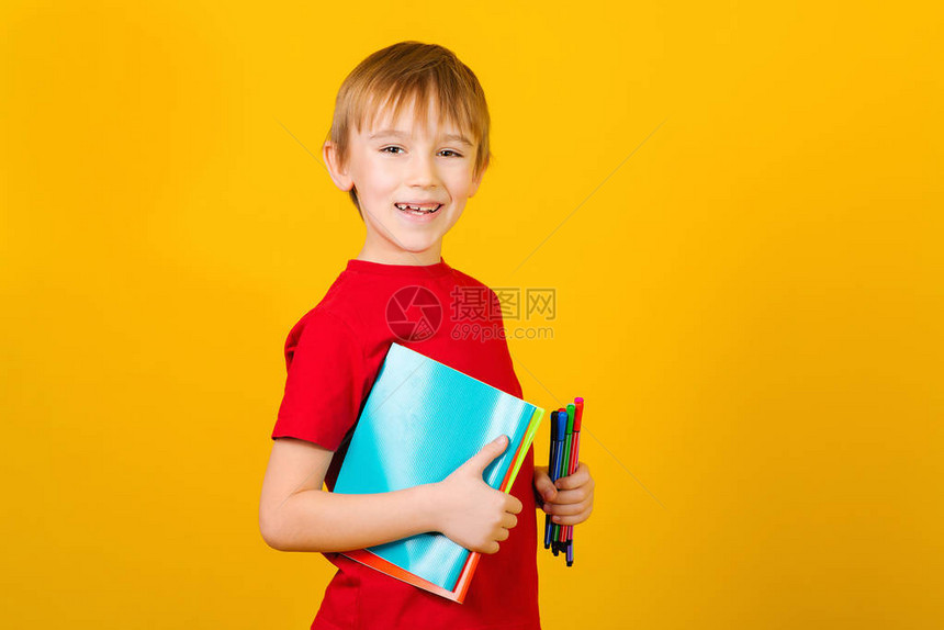 快乐的男孩拿着学校用品在黄色背景有笔记本和笔的孩子回到学校文本的空间图片