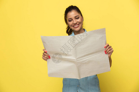 站在黄色工作室背景上时微笑和阅读报纸的正面临时女积图片