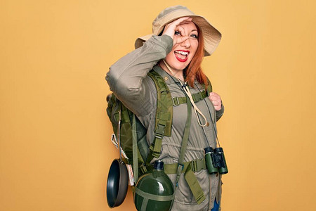 穿着背包和帽子在黄色背景上徒步旅行的年轻红头背心女人图片